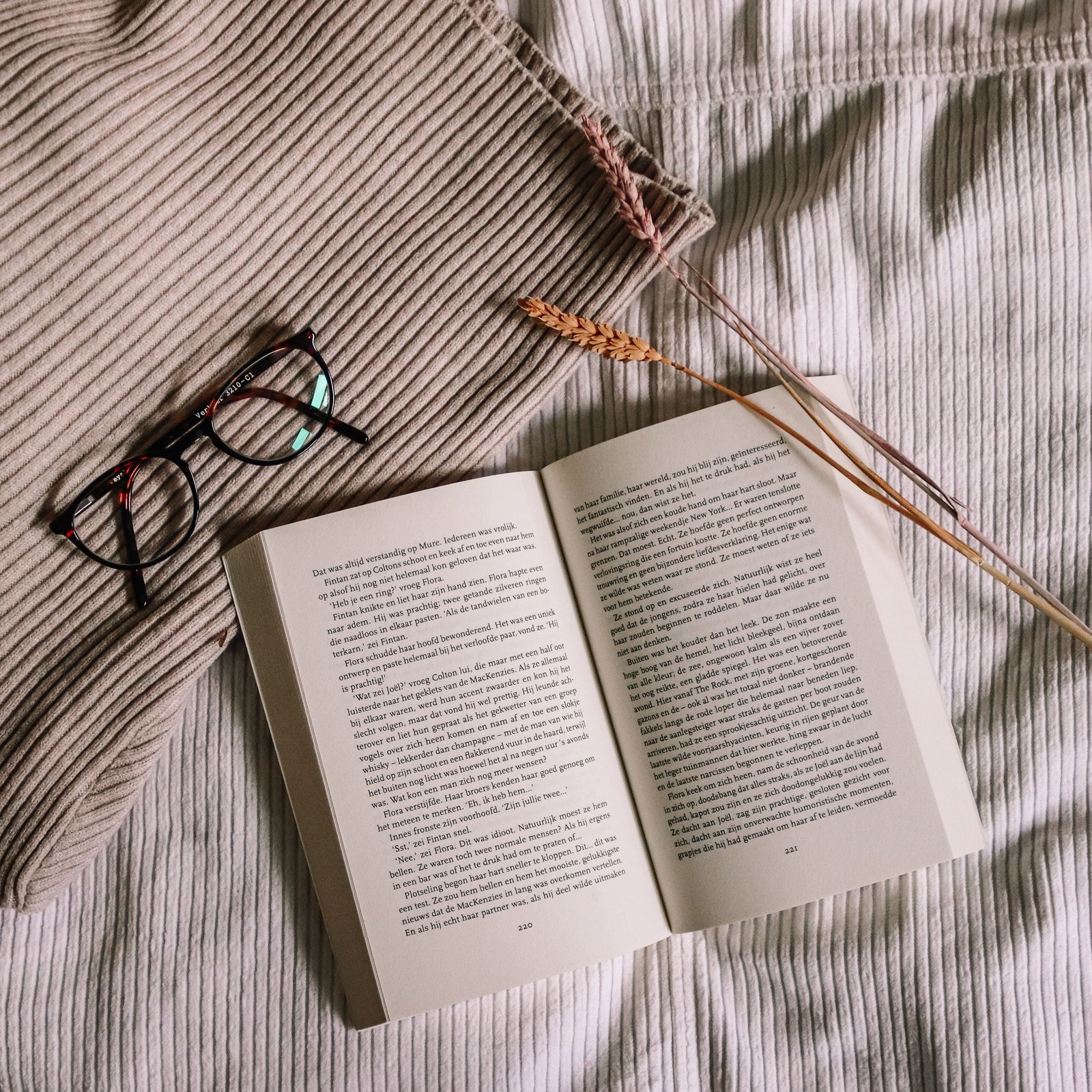 A warm still life of an open book, eyeglasses, and textured blankets creating a cozy reading atmosphere.