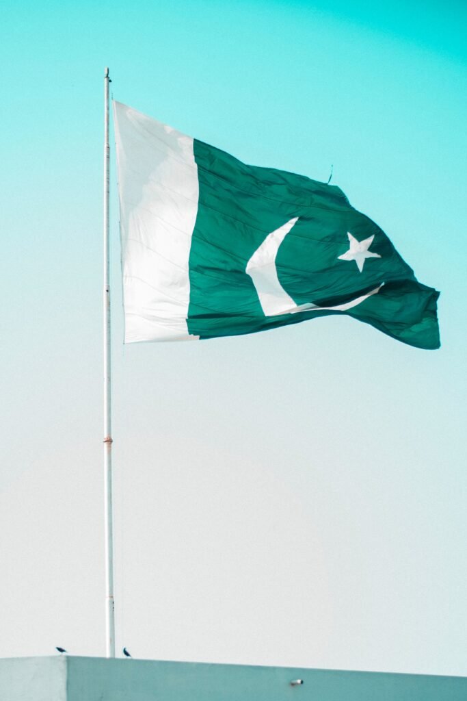 The national flag of Pakistan fluttering in the breeze against a serene blue sky, symbolizing national pride.