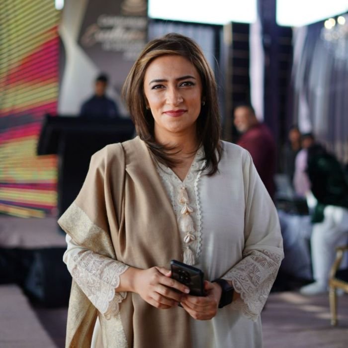 gardener-testimonial-1 Elegant businesswoman holding smartphone, smiling at an event in Dubai. Professional attire and warm ambiance.