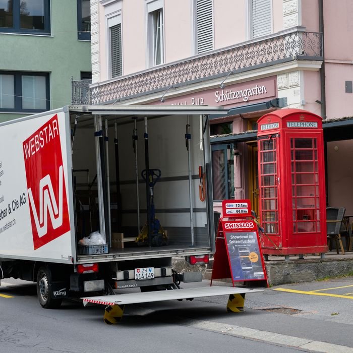 A moving truck parked in front of a Swiss urban venue with a classic red phone booth.