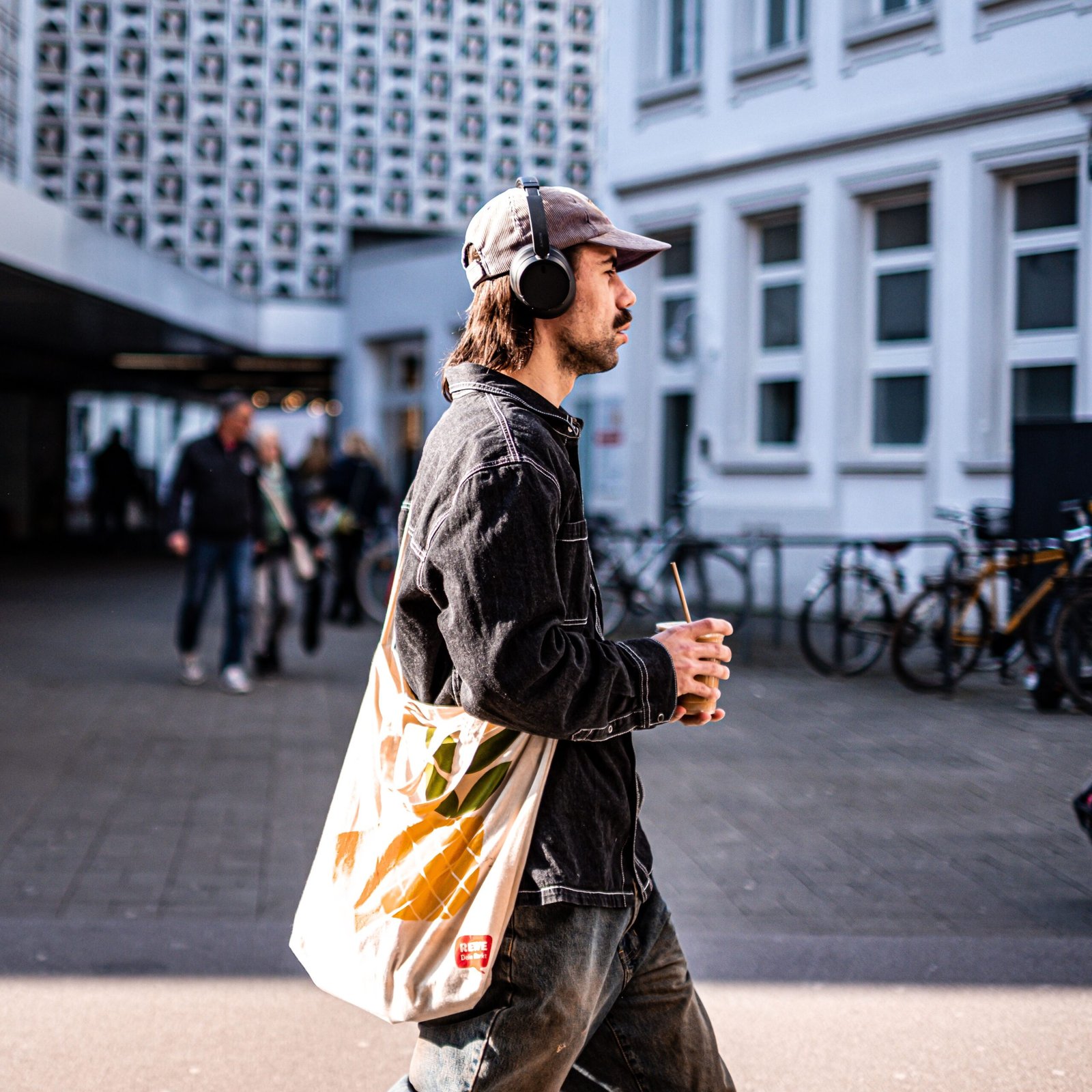 Casual street scene in Trier, Germany, featuring a man with headphones and drink.