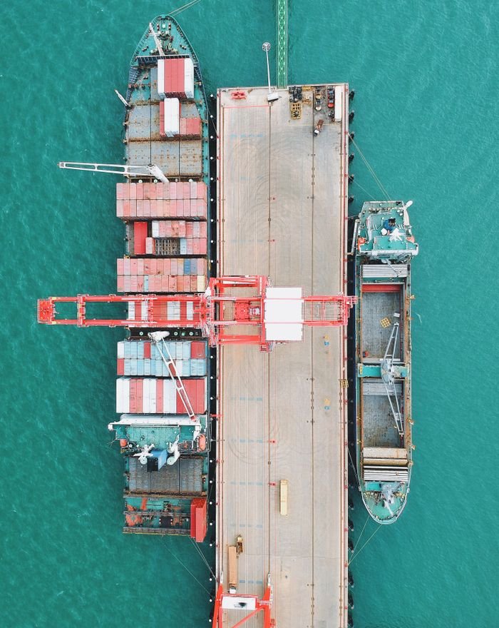 lawn-01 Aerial shot of cargo ships docked at a harbor with cranes and containers.
