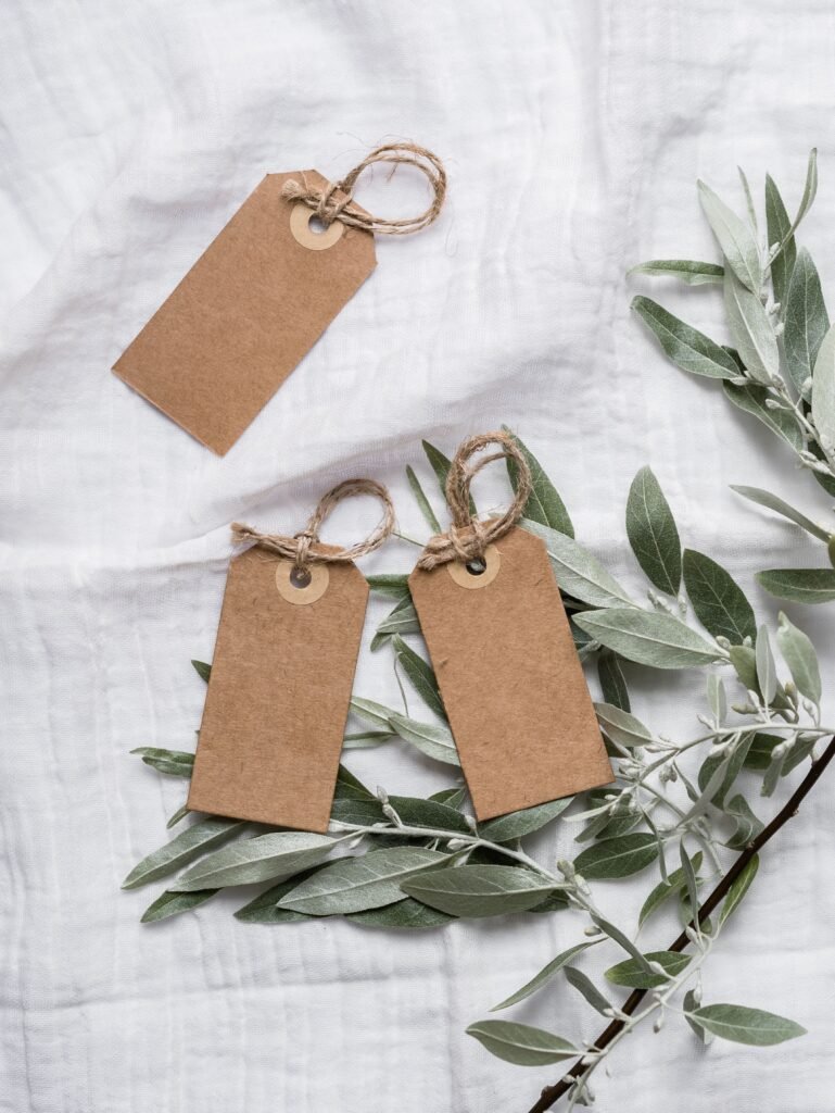 Flat lay of brown paper tags with twine on a white linen cloth, complemented by green leaves.