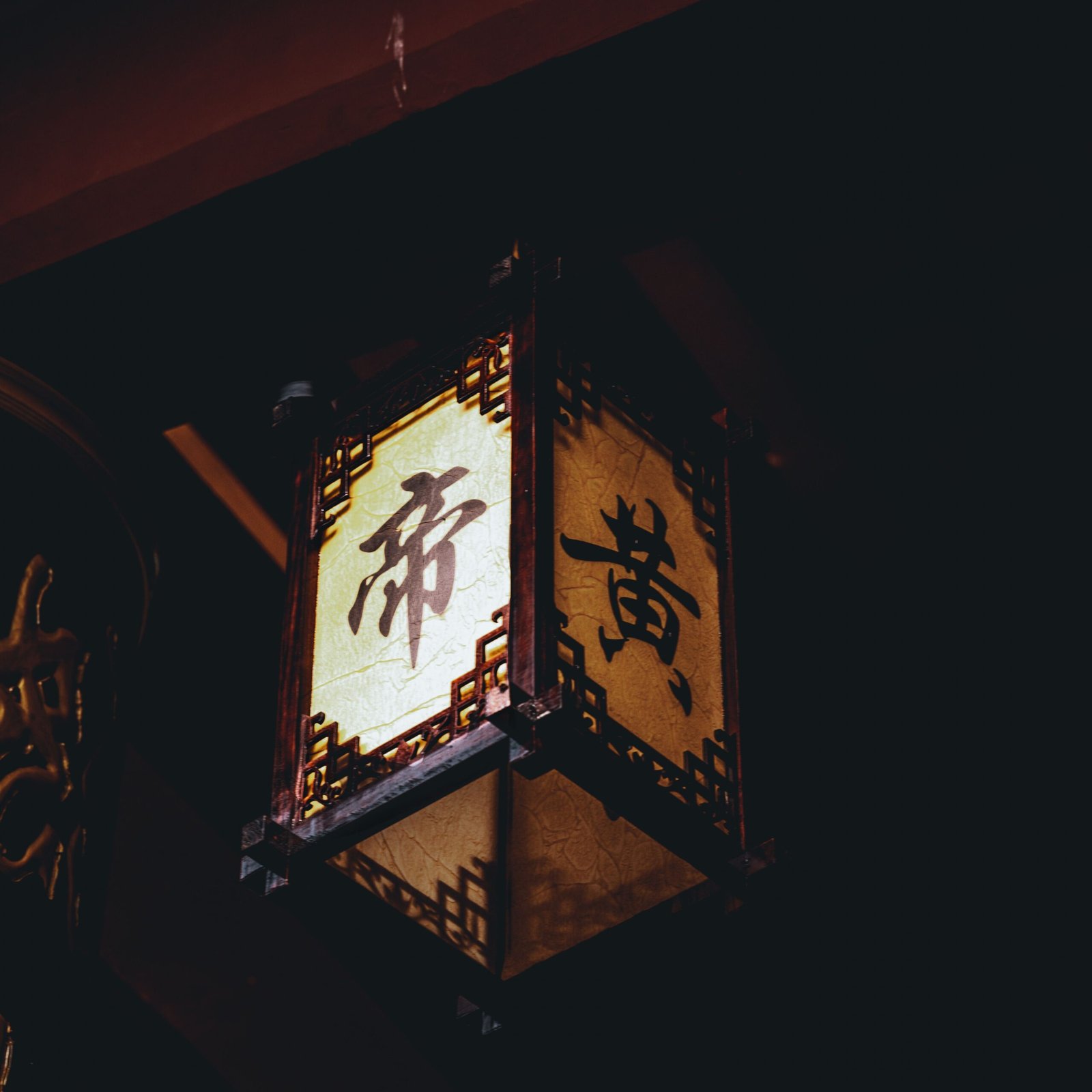 A classic Asian lantern with intricate design hanging in a dim setting, casting warm light.